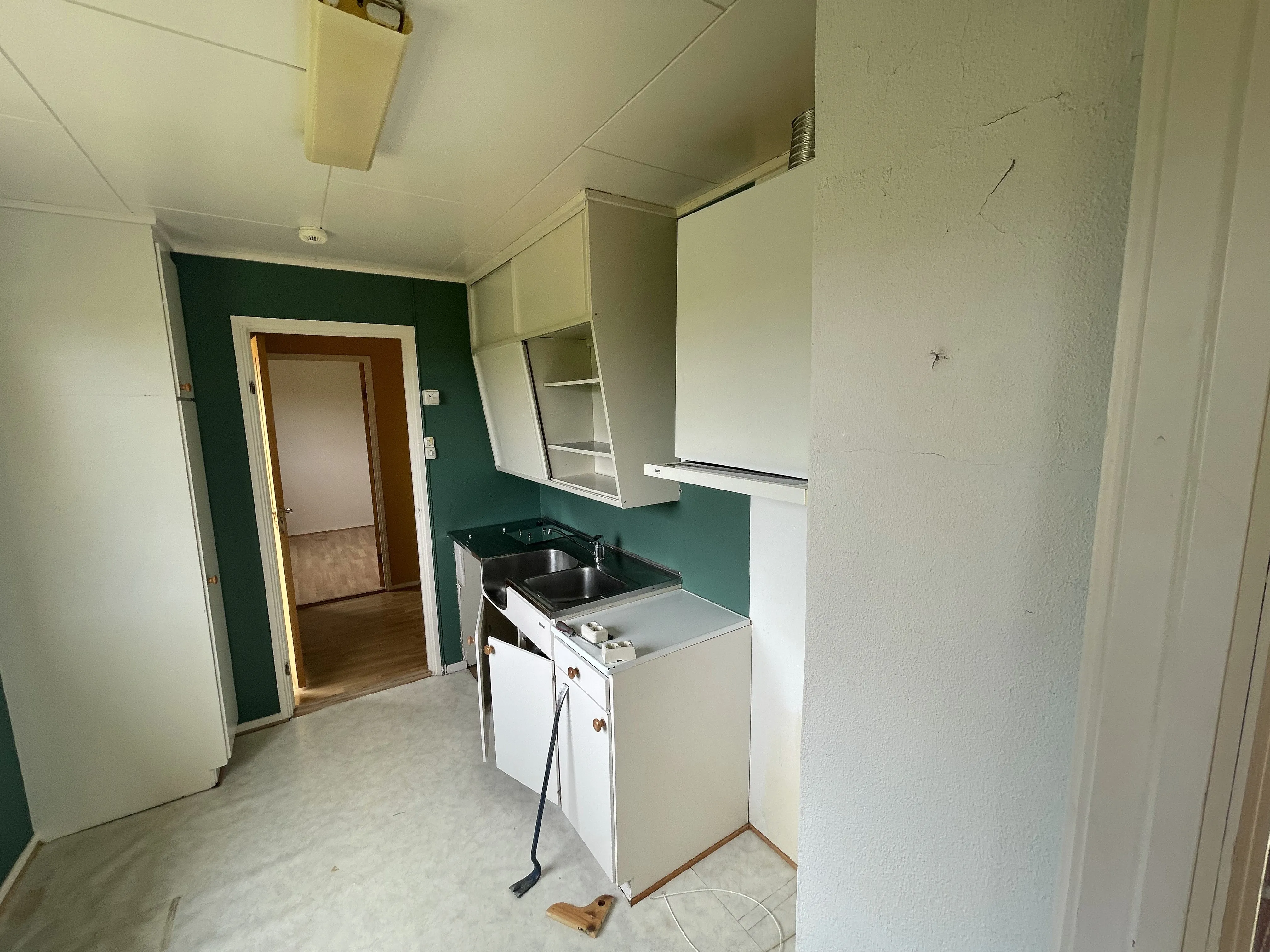 Old kitchen before renovation, with cabinets mid-demolition and a crowbar on the floor.